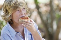 Мальчик с светлыми волосами ест сэндвич на открытом воздухе — стоковое фото