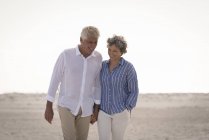 Счастливая старшая пара, идущая по пляжу держа за руки — стоковое фото