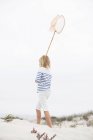 Vista trasera de la niña sosteniendo la red de aterrizaje en la arena en la costa - foto de stock