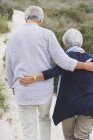 Rear view of embracing senior couple walking on beach — Stock Photo