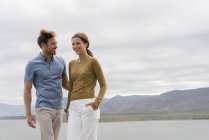 Jovem casal sorrindo se divertindo na margem do lago — Fotografia de Stock