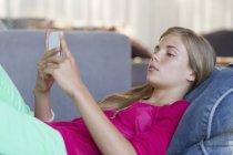 Дівчина-підліток лежить на бобовій сумці і використовує мобільний телефон — стокове фото