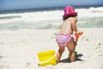 Вид сзади на маленькую девочку, копающую лопатой для песка на пляже — стоковое фото