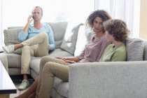 Madre che parla con il figlio sul divano mentre il padre parla al telefono in background in soggiorno a casa — Foto stock