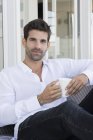 Retrato de hombre feliz disfrutando de la taza de café en el sofá en casa - foto de stock