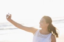 Mujer joven tomando selfie con smartphone en la playa - foto de stock