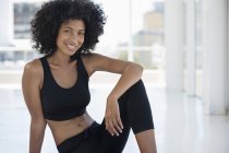 Portrait of smiling sportswoman with afro hairstyle sitting on floor in room — Stock Photo