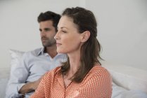 Close-up of thoughtful woman sitting on sofa with husband on background — Stock Photo