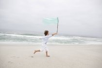 Ragazzo che corre tenendo la bandiera sulla spiaggia di sabbia — Foto stock