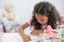 Сфокусированная маленькая девочка делает домашнее задание за столом — стоковое фото