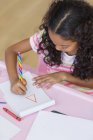 Зосереджена маленька дівчинка робить домашнє завдання за рожевим столом — стокове фото