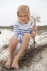 Portrait of smiling girl sitting on sand and holding pinwheel — Stock Photo