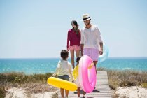 Діти з батьками тримають надувні кільця на дошці на пляжі — стокове фото