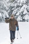 Молодой человек с лыжами на плечах в зимнем лесу — стоковое фото