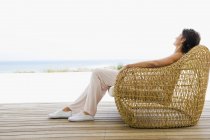 Woman reclining on wicker chair on terrace on coast — Stock Photo