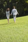 Rear view of couple running on green lawn holding hands — Stock Photo