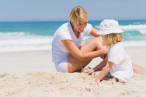 Mujer sentada con su hija en la playa - foto de stock