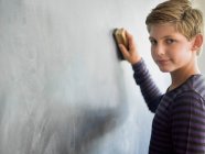 Junge putzt Tafel mit Staubwedel im Klassenzimmer — Stockfoto