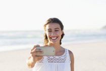 Молодая женщина делает селфи со смартфоном на пляже — стоковое фото