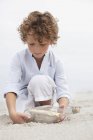 Симпатичный мальчик смотрит на послание в бутылке на песчаном пляже — стоковое фото
