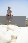 Adolescent garçon à l'aide numérique tablette tandis que assis sur mur à l'extérieur — Photo de stock