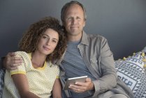 Portrait de couple souriant assis sur le canapé avec tablette numérique — Photo de stock