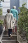 Senior couple carrying suitcases on staircase in front of house — Stock Photo