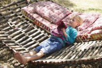 Маленька дівчинка грає з іграшкою, лежачи в гамаку в літньому саду — стокове фото