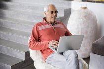 Щасливий старший чоловік використовує ноутбук у кріслі — стокове фото
