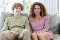 Portrait of happy mother and son sitting on couch in living room — Stock Photo