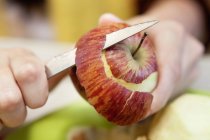 Крупный план человеческих рук, очищающих красное яблоко ножом — стоковое фото