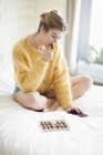 Femme en pull moelleux jaune utilisant le téléphone et manger du chocolat sur le lit — Photo de stock