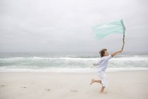 Menino correndo enquanto segurando bandeira na praia de areia — Fotografia de Stock