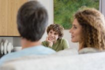 Menino sorrindo falando com os pais enquanto sentado no sofá na sala de estar em casa — Fotografia de Stock