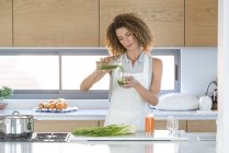 Mujer vertiendo jugo de verduras en el vidrio en la cocina - foto de stock