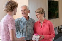 Avós felizes e neto adolescente com presente de aniversário em casa — Fotografia de Stock