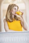 Молода жінка в яскраво-жовтому верхньому випиває апельсиновий сік — стокове фото