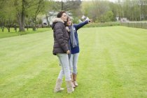Жінка і дочка стоять на осінньому зеленому газоні і вказують — стокове фото