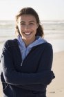 Portrait of young charming woman in warm hoodie standing on beach — Stock Photo