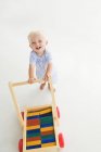 Blond baby boy pushing cart on white background — Stock Photo