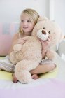 Glückliches kleines Mädchen hält Teddybär auf dem Bett — Stockfoto