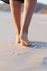 Primer plano de las piernas femeninas caminando en la playa de arena - foto de stock