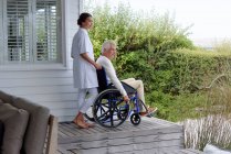 Enfermeira assistente de homem idoso em cadeira de rodas no alpendre — Fotografia de Stock