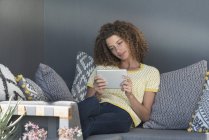 Femme assise sur le canapé à la maison et utilisant une tablette numérique — Photo de stock