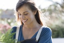 Close-up de sorrir jovem mulher no avental segurando planta no jardim — Fotografia de Stock