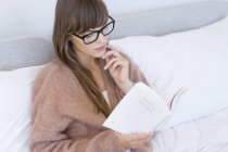 Jovem mulher sentada na cama e ler livro — Fotografia de Stock