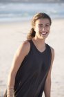 Sorridente giovane donna in top nero in piedi sulla spiaggia — Foto stock