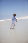 Вид сзади на мальчика, бегущего по песчаному пляжу — стоковое фото