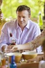 Homem maduro olhando para garrafa de vinho enquanto sentado na mesa do terraço — Fotografia de Stock