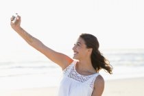 Счастливая молодая женщина делает селфи со смартфоном на пляже — стоковое фото